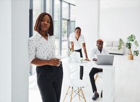 Beautiful woman standing in front of colleagues. Group of african american business people working in office together photo