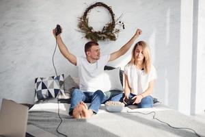 Young lovely couple together at home playing video games on bed with popcorn at weekend time photo