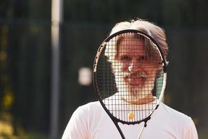 Senior stylish man in white shirt and black sportive shorts on tennis court photo