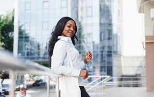 Young afro american woman in white shirt outdoors in the city against business building photo