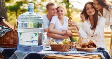 Big plastic water bottle on table. Group of young people have vacation outdoors in the forest. Conception of weekend and friendship photo