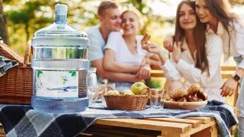 Big plastic water bottle on table. Group of young people have vacation outdoors in the forest. Conception of weekend and friendship photo
