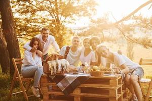 Sitting by picnic table. Group of young people have vacation outdoors in the forest. Conception of weekend and friendship photo