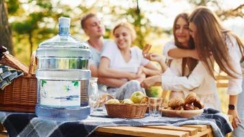 Big plastic water bottle on table. Group of young people have vacation outdoors in the forest. Conception of weekend and friendship photo