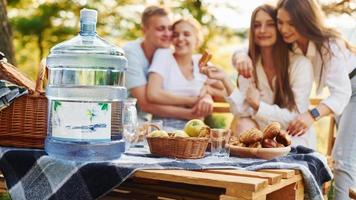 Big plastic water bottle on table. Group of young people have vacation outdoors in the forest. Conception of weekend and friendship photo