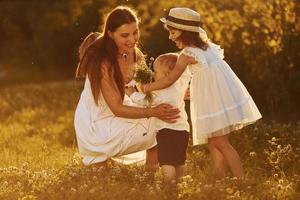 familia feliz de madre, hijo pequeño e hija que pasan tiempo libre en el prado en el día soleado del verano foto