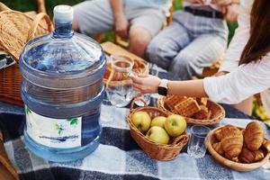 Big plastic water bottle on table. Group of young people have vacation outdoors in the forest. Conception of weekend and friendship photo