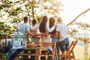 Embracing each other and looking at sunset. Group of young people have vacation outdoors in the forest. Conception of weekend and friendship photo