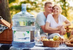 Big plastic water bottle on table. Group of young people have vacation outdoors in the forest. Conception of weekend and friendship photo