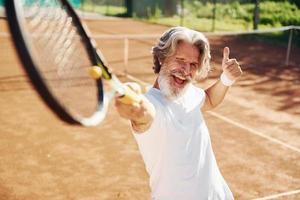 jugando un juego. Senior hombre moderno y elegante con raqueta al aire libre en la cancha de tenis durante el día foto