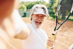 Senior modern stylish man with racket outdoors on tennis court at daytime photo
