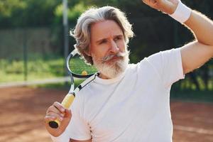Senior modern stylish man with racket outdoors on tennis court at daytime photo