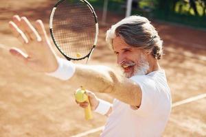 Celebrating victory. Senior modern stylish man with racket outdoors on tennis court at daytime photo