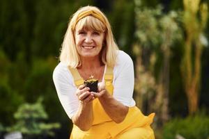 Work day. In yellow colored uniform. Senior woman is in the garden at daytime. Conception of plants and seasons photo