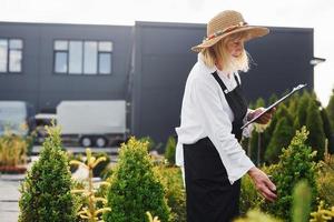 Notepad in hands. Senior woman is in the garden at daytime. Conception of plants and seasons photo