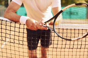 vista de cerca del anciano con camisa blanca y pantalones cortos deportivos negros que está en la cancha de tenis