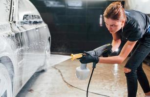 Using high pressure water. Modern black automobile get cleaned by woman inside of car wash station photo