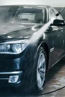 High pressured water. Modern black automobile get cleaned inside of car wash station photo