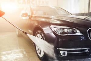 High pressured water. Modern black automobile get cleaned inside of car wash station photo