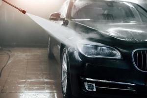 High pressured water. Modern black automobile get cleaned inside of car wash station photo