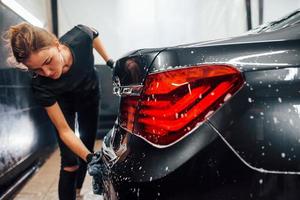 Close up view of vehicle getting wiped. Modern black automobile get cleaned by woman inside of car wash station photo