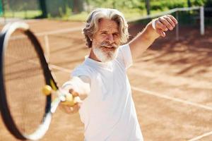 Playing game. Senior modern stylish man with racket outdoors on tennis court at daytime photo