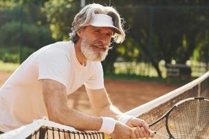 Senior hombre moderno y elegante con raqueta al aire libre en la cancha de tenis durante el día