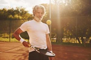 Training time. Senior modern stylish man with racket outdoors on tennis court at daytime photo