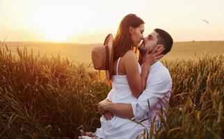 Lovely couple kissing and spending free time on the field at sunny day time of summer photo