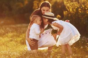 familia feliz de madre, hijo pequeño e hija que pasan tiempo libre en el prado en el día soleado del verano foto