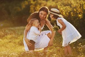 Happy family of mother, little son and daughter spending free time on the meadow at sunny day time of summer photo