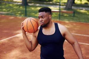 hombre afroamericano de pie con pelota en la cancha al aire libre foto