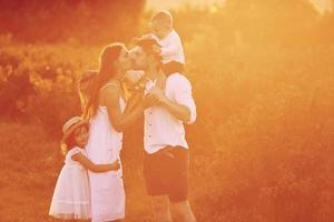 Illuminated bu sunlight. Family of four people spending free time on the field at day time of summer photo