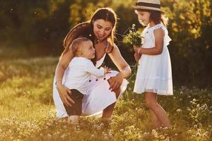 Happy family of mother, little son and daughter spending free time on the meadow at sunny day time of summer photo