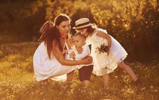 Cheerful family of mother, little son and daughter spending free time on the field at sunny day time of summer photo