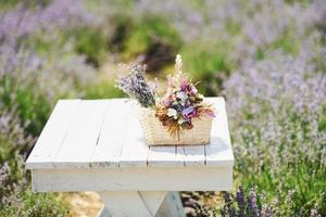 Close up view of bouquet of lavender flowers in basket that lying on the white table in field photo