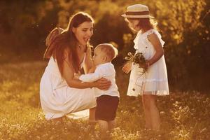 Cheerful family of mother, little son and daughter spending free time on the field at sunny day time of summer photo