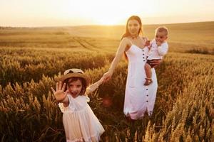 Cheerful family of mother, little son and daughter spending free time on the field at sunny day time of summer photo