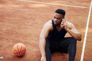 habla por teléfono. hombre afroamericano juega baloncesto en la cancha al aire libre