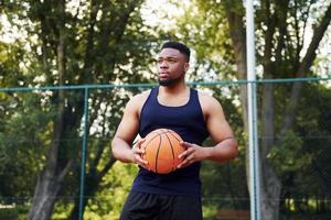 hombre afroamericano de pie con pelota en la cancha al aire libre foto