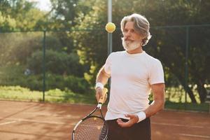 Training time. Senior modern stylish man with racket outdoors on tennis court at daytime photo