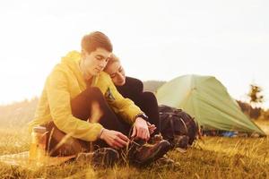 Young lovely couple sitting near tent outdoors at daytime. Beautiful sunlight photo