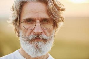 Portrait of seenior stylish man with grey hair and beard that standing outdoors on field at sunny day photo