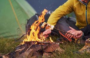 Close up view of people's hands that holds sticks with marshmallow outdoors near campfire photo