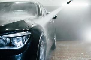 High pressured water. Modern black automobile get cleaned inside of car wash station
