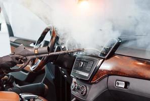 Modern black automobile get cleaned inside by steam equipment by worker inside of car wash station photo