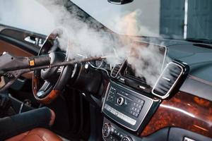 Modern black automobile get cleaned inside by steam equipment by worker inside of car wash station photo