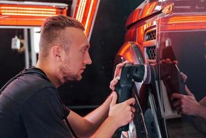 Guy polishing surface of vehicle. Modern black automobile get cleaned by man inside of car wash station photo