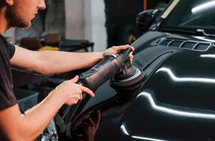 Guy polishing surface of vehicle. Modern black automobile get cleaned by man inside of car wash station photo