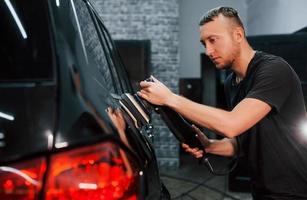 Guy polishing surface of vehicle. Modern black automobile get cleaned by man inside of car wash station photo